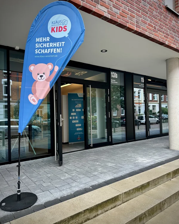 Eingang des Kieler Büros in der Christian-Kruse-Straße 13b mit geöffneter Glastür und Beachflag von Klaus versichert